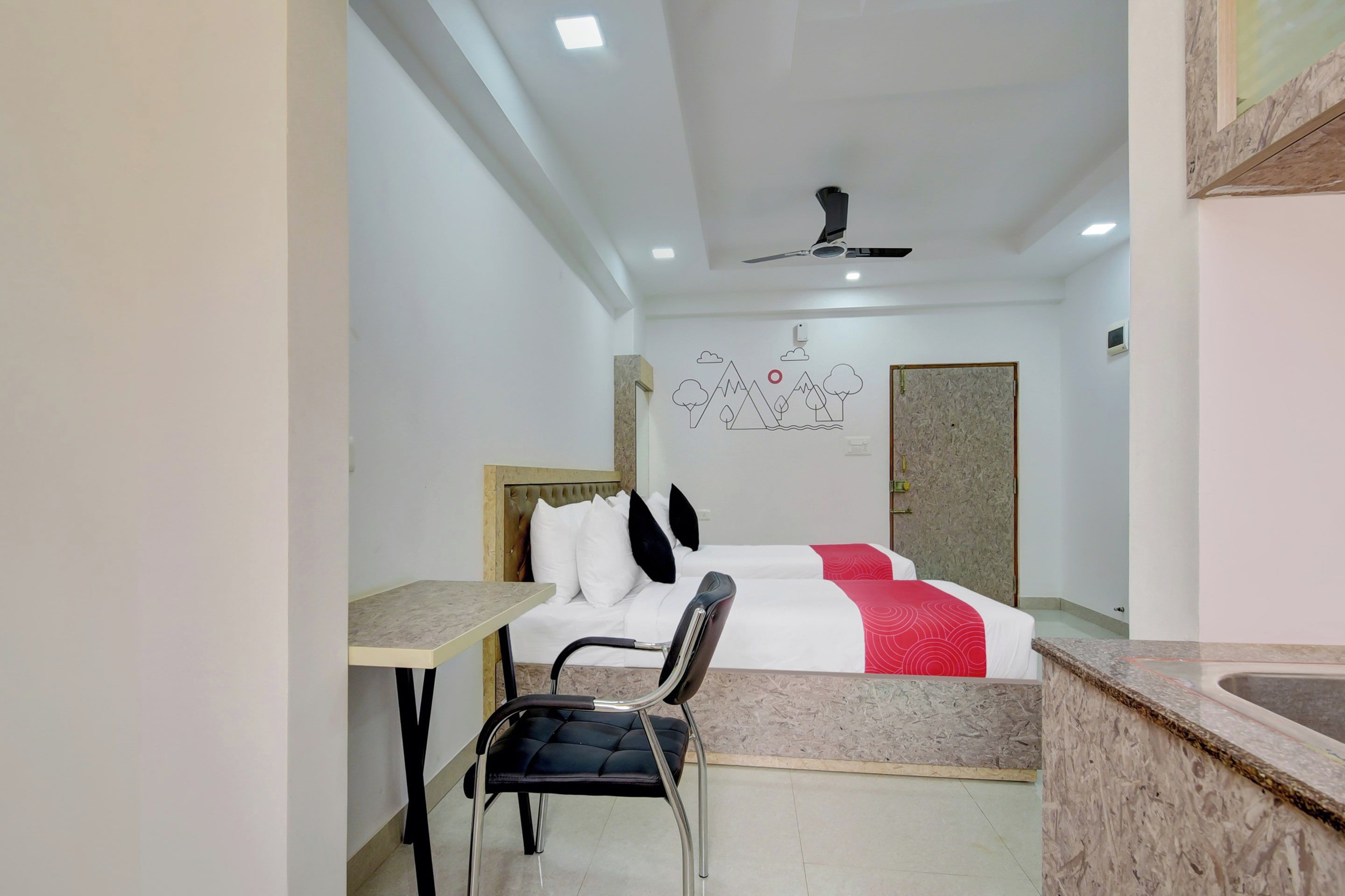 Habitación de hotel con una cama, un escritorio, una silla, un ventilador de techo y una pared con un diseño de montaña.