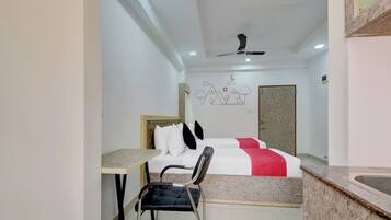 Habitación de hotel con una cama, un escritorio, una silla, un ventilador de techo y una pared con un diseño de montaña.