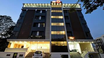 A multi-story hotel with illuminated signage, a visible entrance, and a car parked in front.