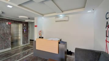 Zona de recepción con pared de mármol, un ascensor, un extintor y un sofá gris.