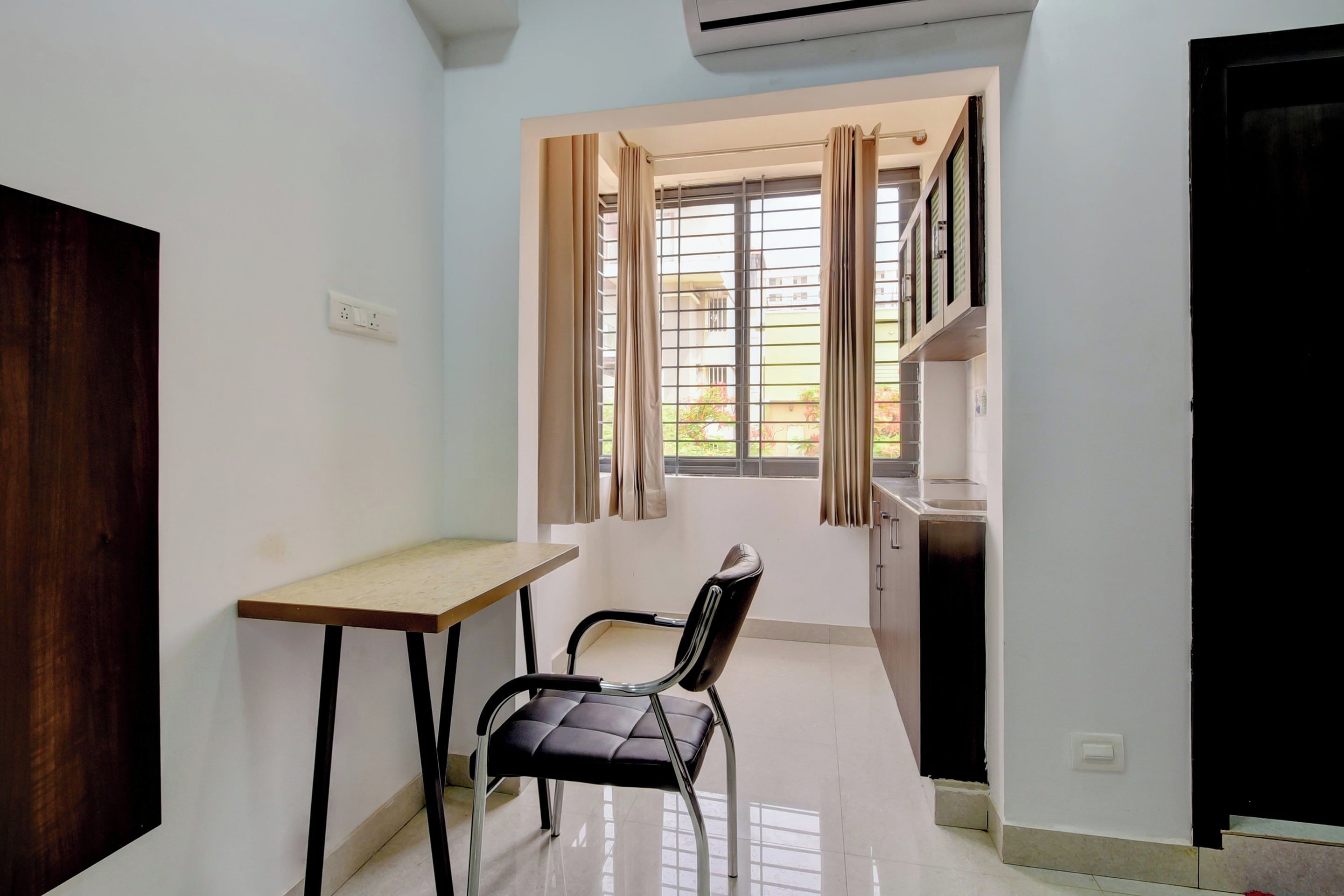 A small room with a desk, a chair, a window with curtains, and a door.