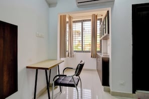 Una habitación pequeña con un escritorio, una silla, una ventana con cortinas y una puerta.