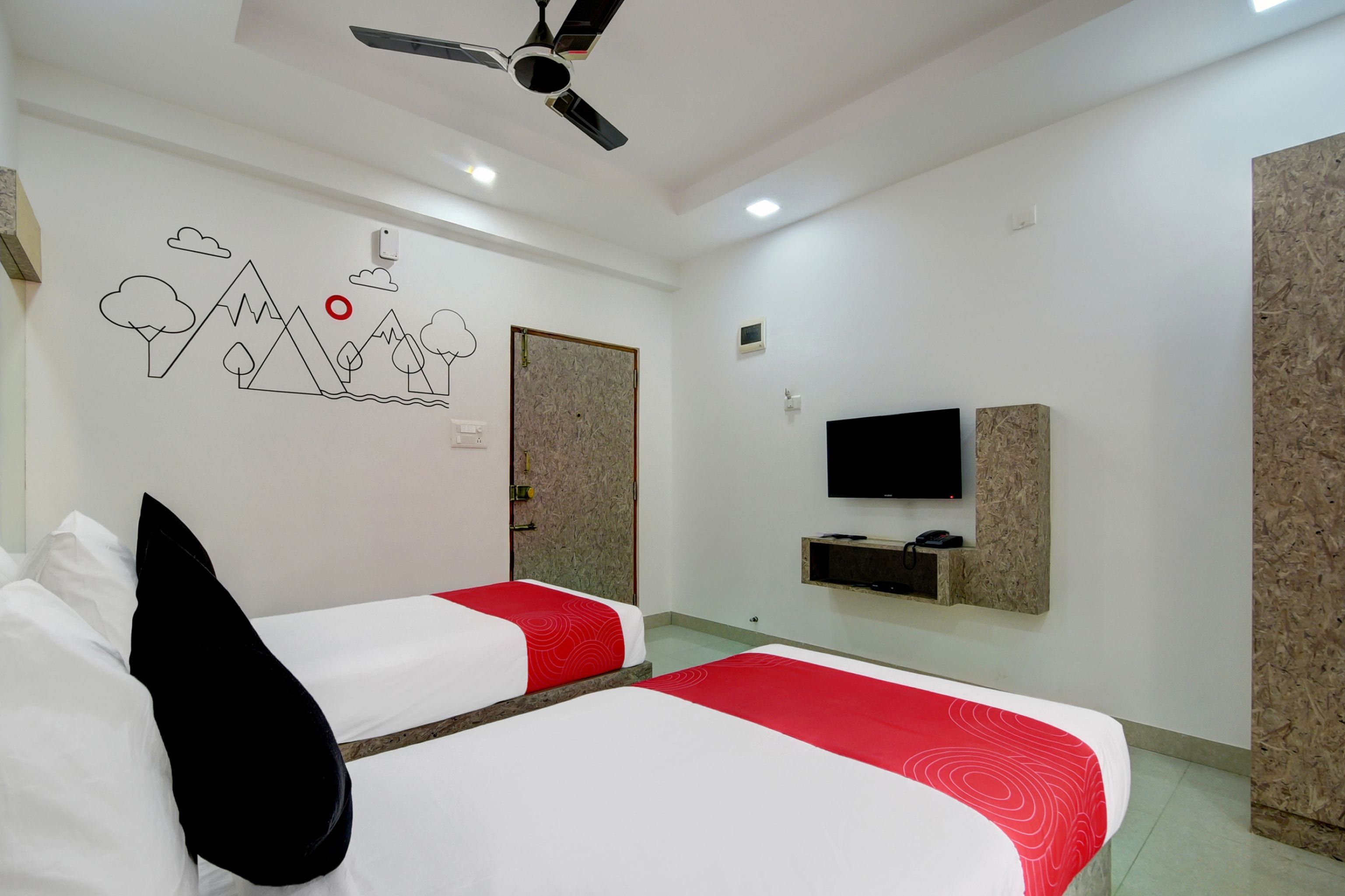 Habitación de hotel con dos camas, ventilador de techo, televisión y estante en la pared.