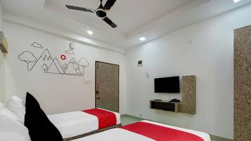 Habitación de hotel con dos camas, ventilador de techo, televisión y estante en la pared.
