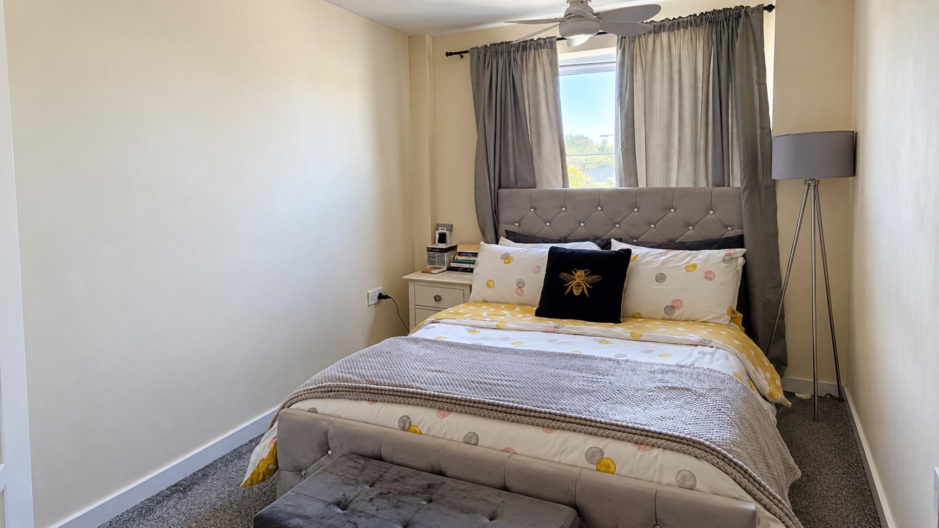 Un dormitorio con una cama, una mesita de noche, una lámpara y un ventanal con cortinas.