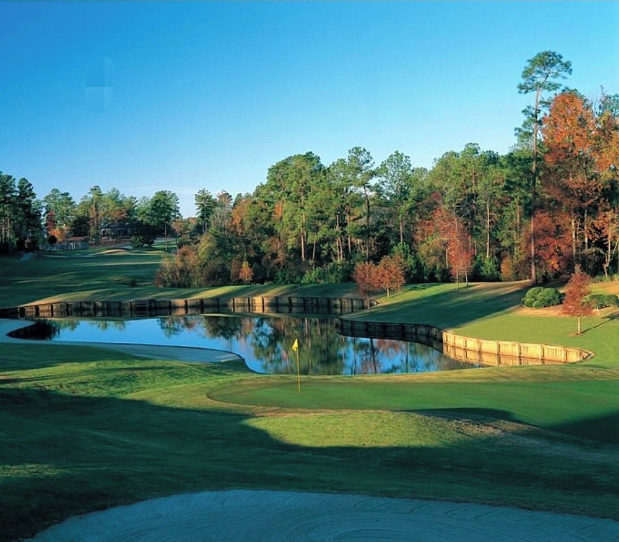 A golf course with a pond, trees, and a clear sky.