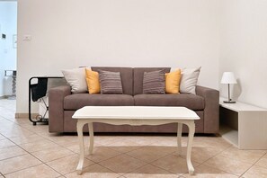Ein Wohnzimmer mit einer Couch, einem weißen Tisch, einer Lampe und einem Rollwagen.