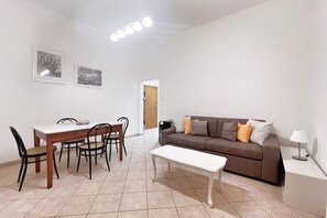 A living room with a brown sofa, a white coffee table, and a dining area with a table and chairs. - UR NEST Toscana - One bedroom apartment inside a gracious villetta (Bologna)