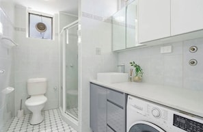 Un bagno moderno con un WC, una doccia, un lavandino e una lavatrice.