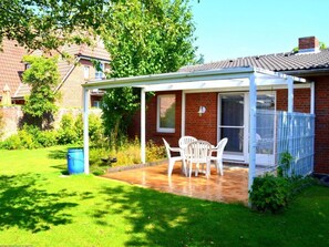 A covered patio with a table and chairs, a brick house, and a fenced area. - "rungholtstrasse" (Wyk auf Foehr)
