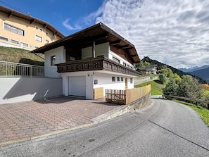 Ein zweistöckiges Haus mit Balkon, Auffahrt und einer nach rechts führenden Straße.