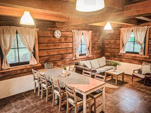 L’intérieur d’un chalet accueillant, avec une table à manger en bois, des chaises, un canapé et une horloge au mur.