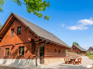 A wooden cabin with a sloped roof, a stone foundation, and a gravel driveway.