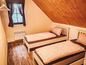 A room with two single beds, a window with curtains, a radiator, and wooden flooring.