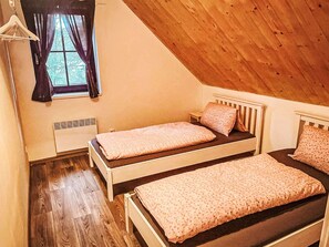 Une chambre avec deux lits simples, une fenêtre avec des rideaux, un radiateur et un plancher en bois.