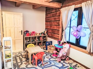 Une salle de jeux pour enfants avec un plancher en bois, une petite table, une chaise, une voiture jouet et une poussette.