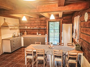 A rustic kitchen with wooden cabinets, a dining table, and chairs. There is a window providing a view of the outdoors.