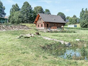 Une cabane rustique en rondins de bois, dotée d’un toit en pente, entourée d’un champ verdoyant et d’un petit étang.