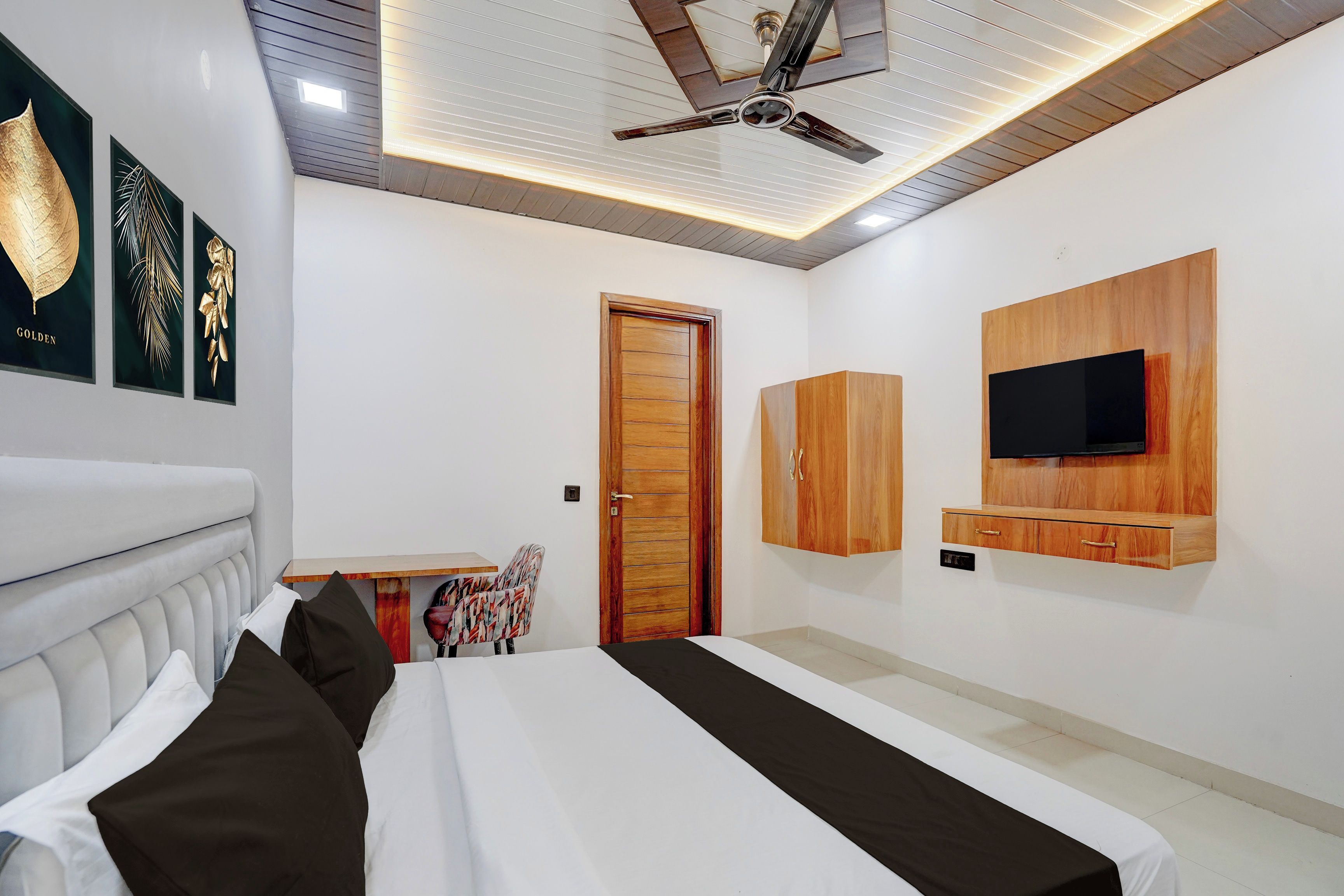 Ein modernes Schlafzimmer mit einem Bett, einem Deckenventilator, einem an der Wand montierten Fernseher und einer Tür.