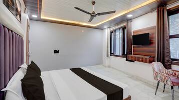 Una habitación de hotel con una cama, una silla, un televisor y un ventilador de techo.