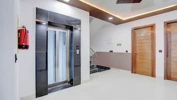 A modern elevator with a glass panel, a fire extinguisher mounted on the wall, and a staircase leading to an upper floor.