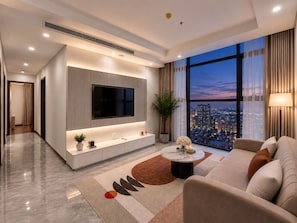 Ein modernes Wohnzimmer mit Flachbildfernseher, einer Couch, einem Couchtisch und Blick auf eine Stadtlandschaft im Abendlicht.