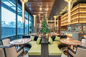 A modern dining area with a Christmas tree, seating arrangements, and a view of the city. - Nancy Apartment Capital Elite - My Dinh (Tu Liem Ward)