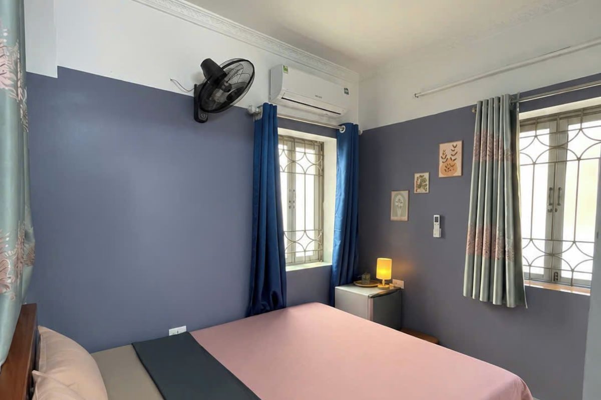 Quarto com uma cama, mesa de cabeceira com abajur, ventoinha e ar condicionado.