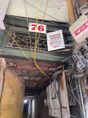 Quarto desarrumado com fiação elétrica exposta, um letreiro indicando o preço de 76 e um anúncio de serviço de hospedagem em domicílio.