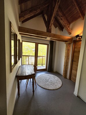 Ein Zimmer mit einem Holztisch und -stühlen, einem runden Teppich und Blick durch ein großes Fenster auf eine Terrassenanlage.