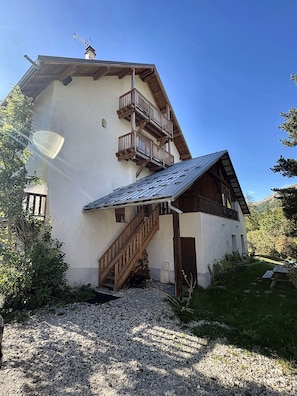 Ein Gebäude mit einer Holztreppe, die zu einem Balkon führt, umgeben von Kies und Grünpflanzen.
