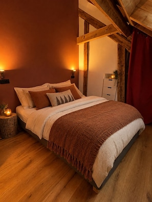 Ein Schlafzimmer mit Holzboden, einem Bett mit brauner Decke, zwei Wandleuchten und einem Nachttisch mit Kerze.