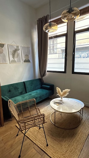 A room with a green sofa, a wicker chair, a round table with a white top, and a hanging light fixture. - FER’s SPOT beautiful studio/apartment downtown Madrid close to all imprtnt spots (Madrid)