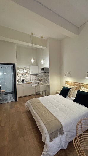 A modern bedroom with a large bed, bedside lamps, and a view of a compact kitchen area. - FER’s SPOT beautiful studio/apartment downtown Madrid close to all imprtnt spots (Madrid)
