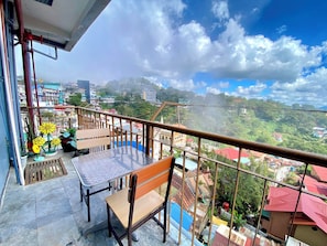 A balcony with a table and chair, overlooking a residential area with houses and greenery.
