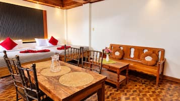 A room with a wooden dining table, chairs, a sofa, and a bed with red pillows.