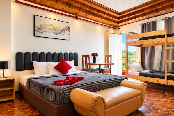 A hotel room with a bed, a desk, a chair, a sofa, a bunk bed, and a painting on the wall.