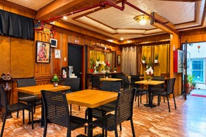 A restaurant interior with wooden paneling, black perforated chairs, and a marble floor.