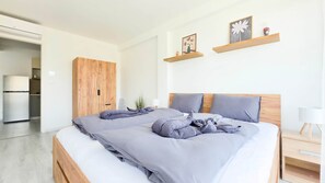 A modern bedroom with a bed, wooden wardrobe, and a kitchenette. - LB - Balcsikuckó Apartman (Siófok)
