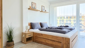 Quarto moderno com cama de madeira, mesas de cabeceira, um criado-mudo, planta em vaso e janela com vista para edifícios.