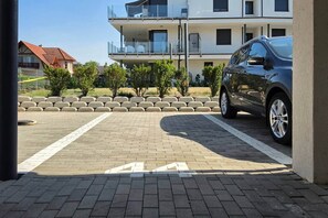 Un espace de stationnement avec une voiture, recouvert de pavés, et une rangée de petits arbres.