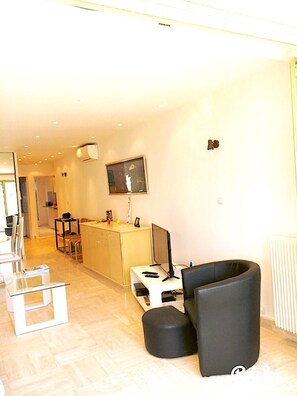 A modern living room with a flat-screen TV, a black sofa, a glass coffee table, and a dining area with chairs. - Beautiful apartment facing the sea—Croisette Immo (Cannes)