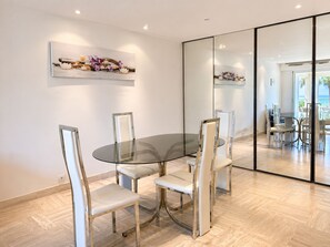 A modern dining area with a glass table and metal chairs, a wall-mounted artwork, and a large mirror reflecting the space. - Beautiful apartment facing the sea—Croisette Immo (Cannes)