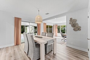A modern dining area with a wooden table, patterned chairs, and a hanging light fixture. - Charming Delray Beach Home in Lake Ida (Delray Beach)