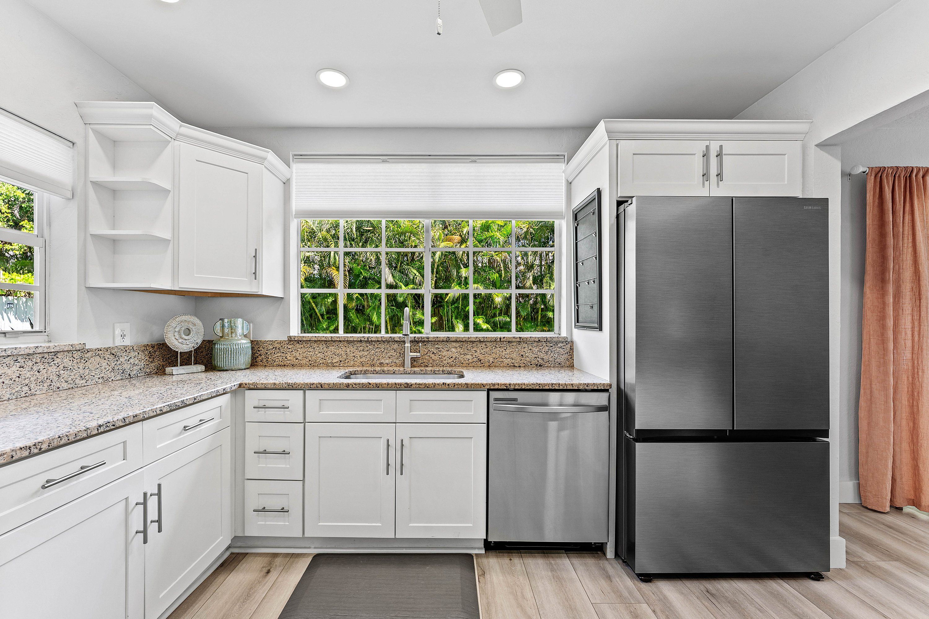 A modern kitchen with white cabinetry, a stainless steel refrigerator, and a window with a view of greenery.