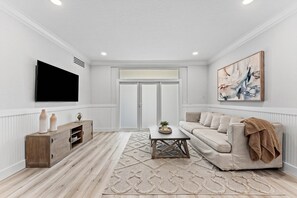 A living room with a flat-screen TV, a sofa, a coffee table, and a painting on the wall. - Charming Delray Beach Home in Lake Ida (Delray Beach)
