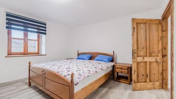 A bedroom with a wooden bed, a nightstand, a window with blinds, and a wooden door.