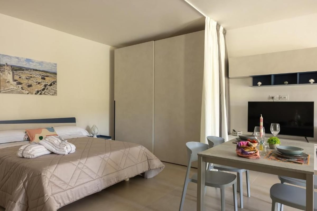 Ein Hotelzimmer mit einem Bett, einem Esstisch mit Stühlen, einem Fernseher und einem Bild an der Wand.