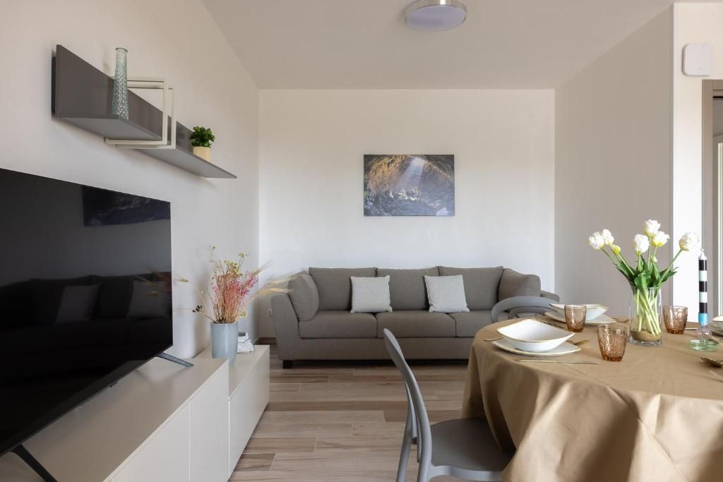 Un soggiorno moderno con una TV a schermo piatto, un divano grigio e un'area pranzo con un tavolo apparecchiato per due.