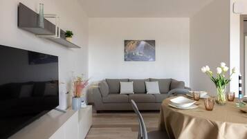 Un soggiorno moderno con una TV a schermo piatto, un divano grigio e un'area pranzo con un tavolo apparecchiato per due.